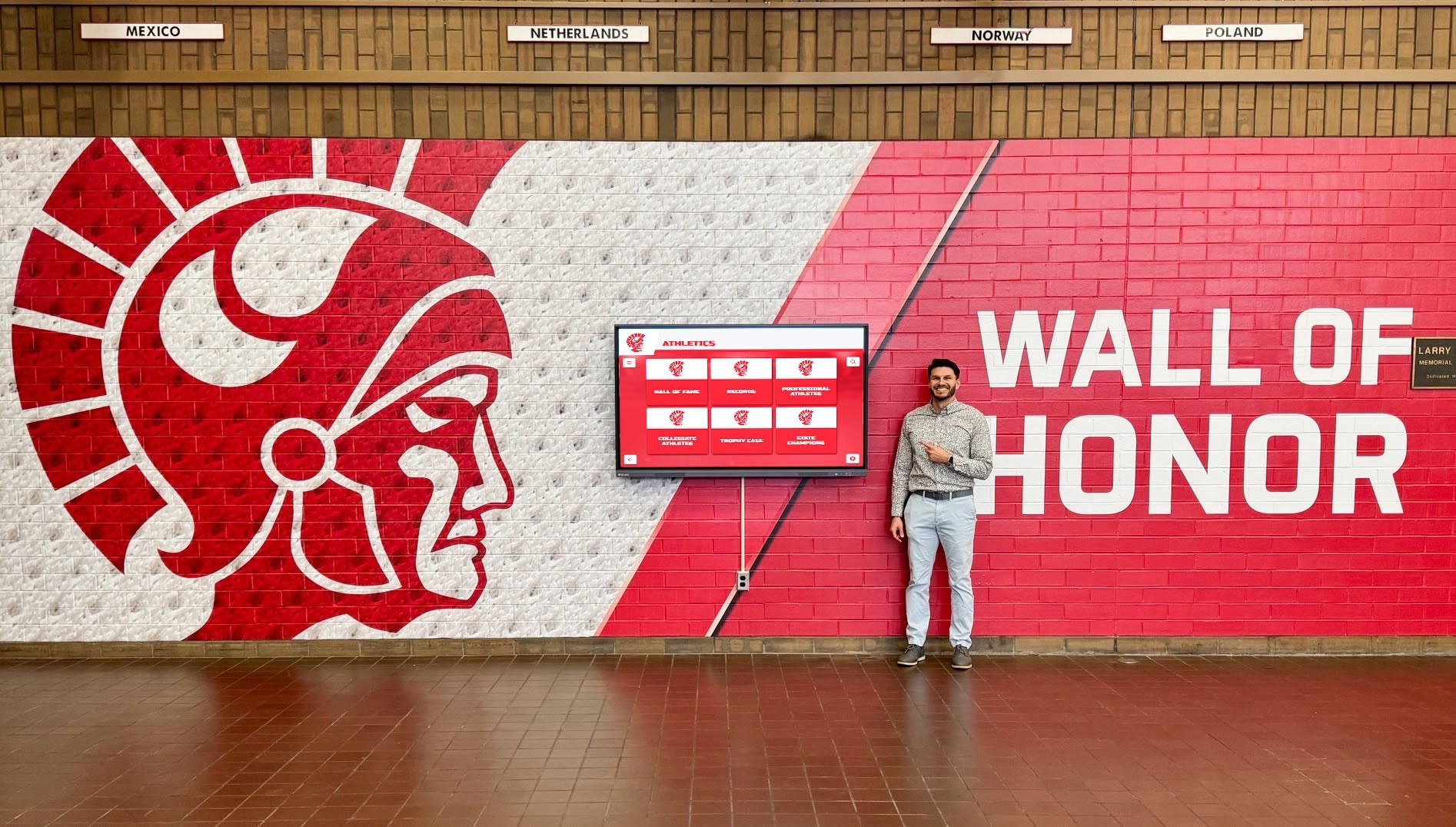 Visitor engaging with alumni wall of honor in school hallway